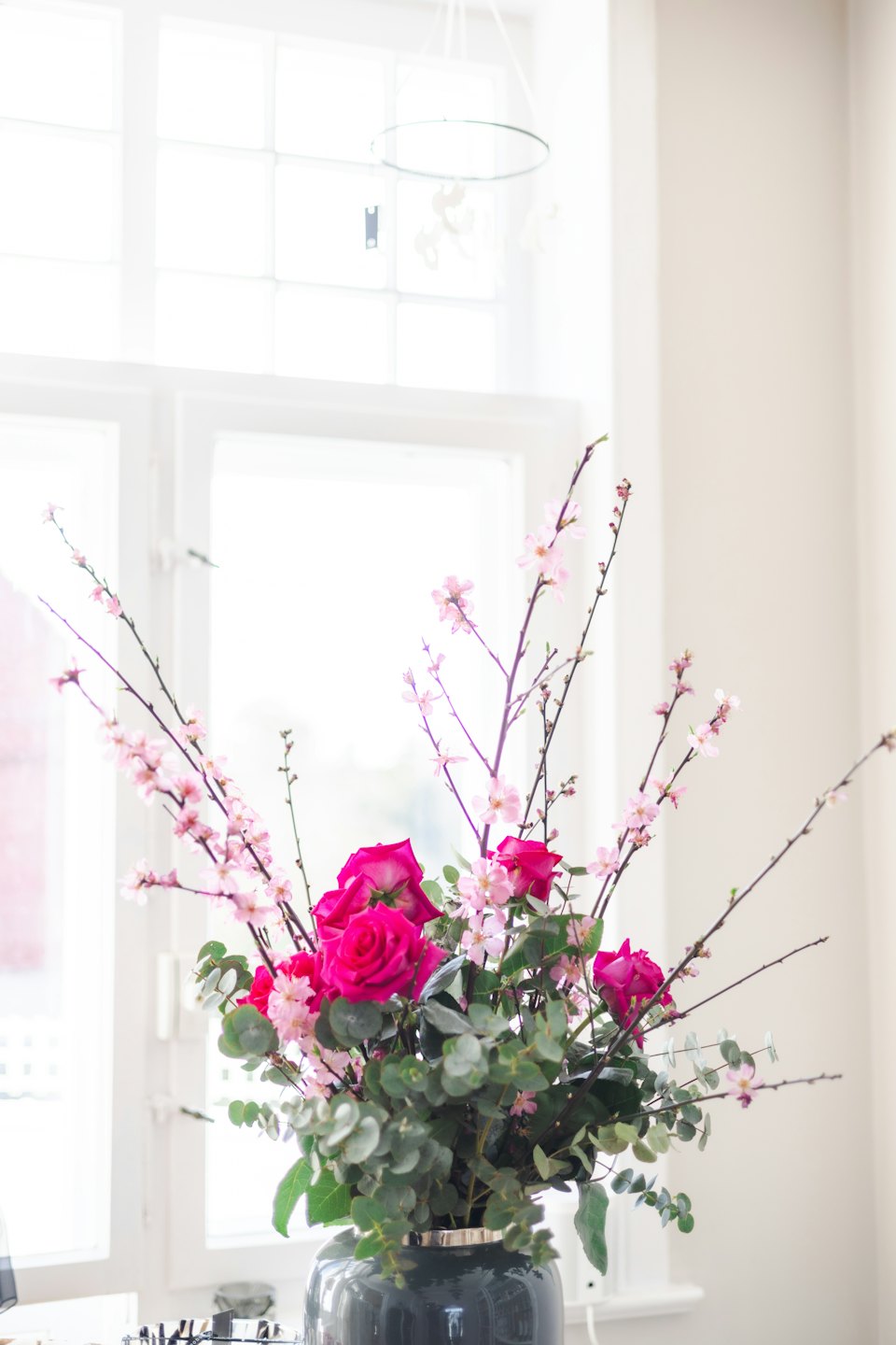 Pink roses and eucalyptus branches in a grey ceramic vase.