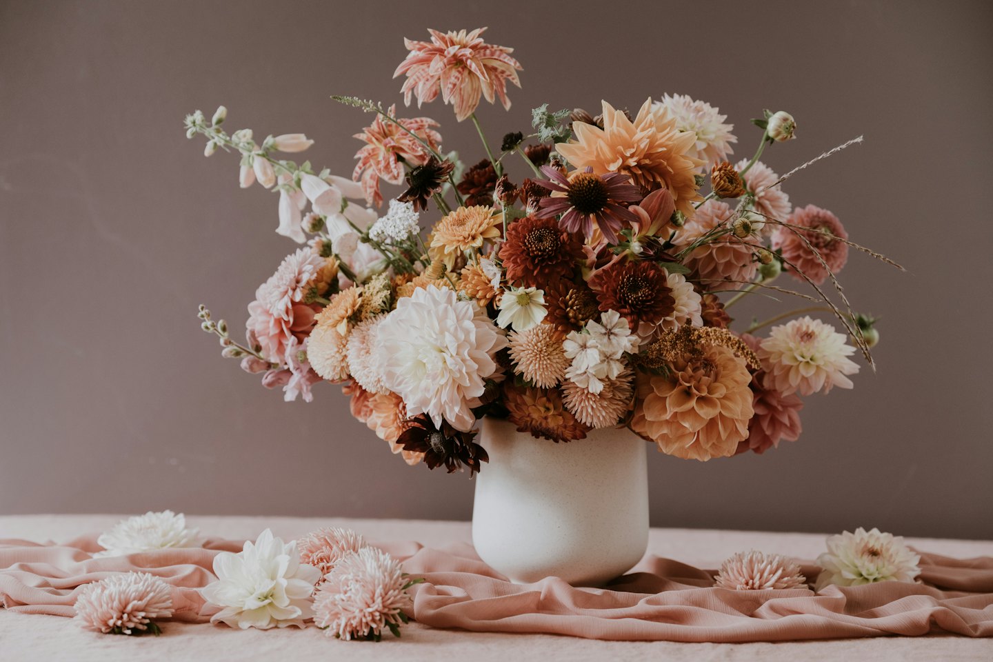 Dahlias and mixed greenery sit in a white ceramic vase.