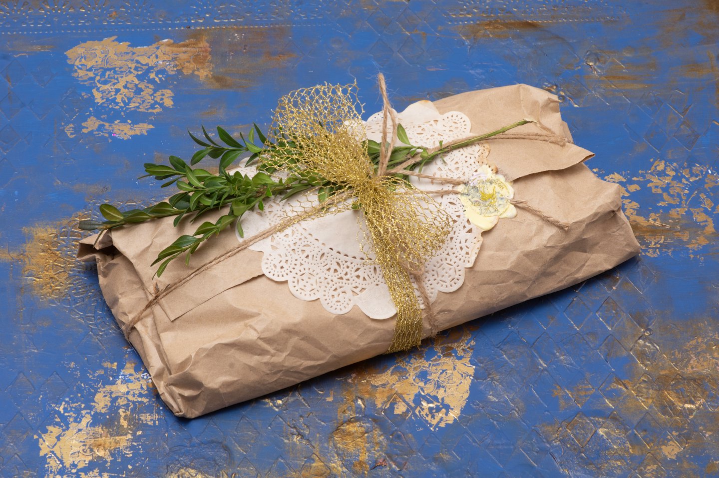 Gift wrapped in kraft paper with doily and greens on blue surface.